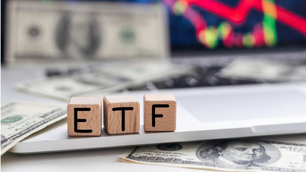 A inscrição do fundo negociado em bolsa (ETF), escrita em cubos de madeira, com um gráfico e dinheiro em segundo plano