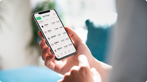 Uma pessoa utiliza um iPhone para efetuar uma transação na aplicação xStation da XTB, mostrando a interface da aplicação e as funcionalidades de negociação digital