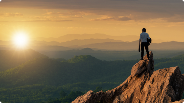 Osoba na vrcholu hory, obdivující výhled na západ slunce